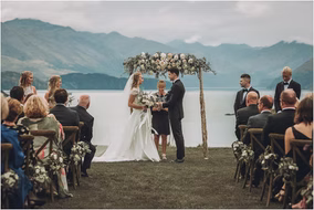Bride and groom hold hands at the altar beneath a floral arch during their lakeside wedding ceremony in Michigan.