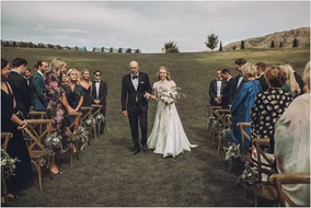 Father walks his daughter down the aisle while guests look on at this beautiful outdoor wedding in Michigan.