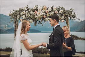 Bride and groom exchange vows under a flower-adorned arch at their intimate Michigan lake wedding.